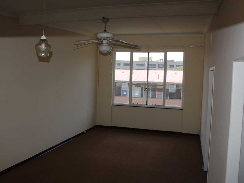 An empty living room featuring a ceiling fan, pendant lighting, and a large window, providing a blank canvas for potential renovation and interior design.