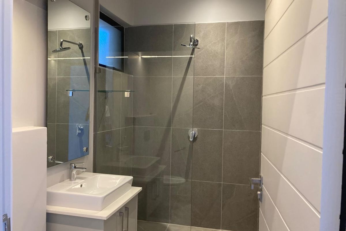 Modern bathroom featuring a sleek vanity with ceramic basin, large wall mirror, and a spacious walk-in shower with grey tiled finishes.