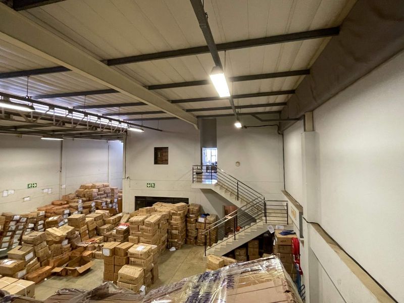 A large industrial warehouse space featuring high ceilings with exposed steel trusses, a central staircase, and functional fire safety equipment.