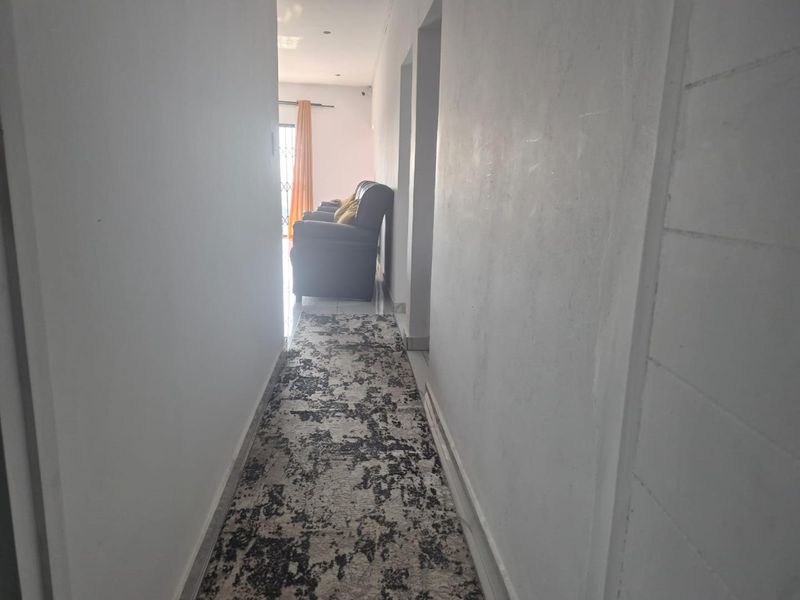 A narrow residential hallway featuring tiled flooring and recessed lighting, leading towards an open living area.