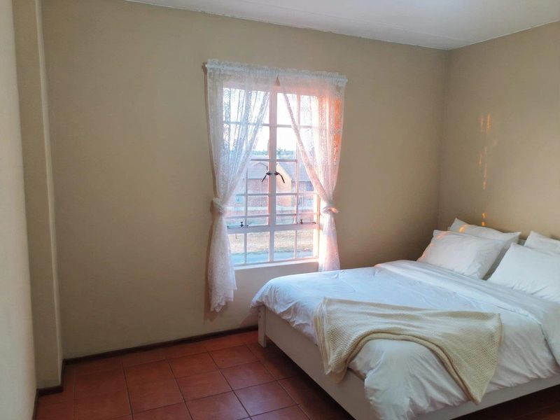 A simple bedroom featuring tiled flooring and a window with natural light.