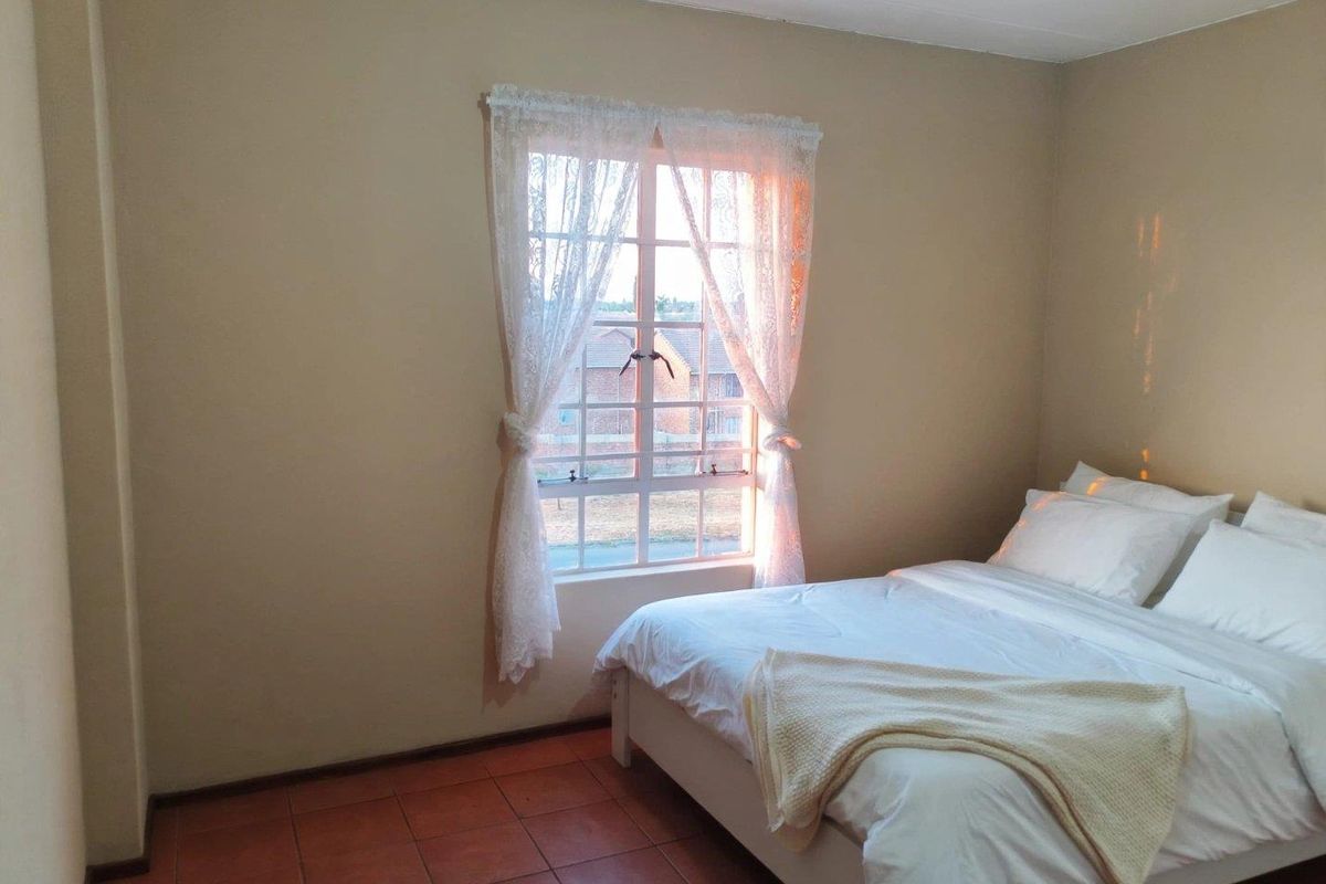 A simple bedroom featuring tiled flooring and a window with natural light.