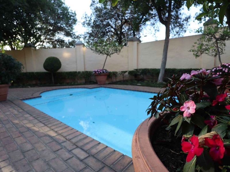 A private swimming pool area featuring paved surrounds and a high perimeter boundary wall, set within a landscaped garden environment.