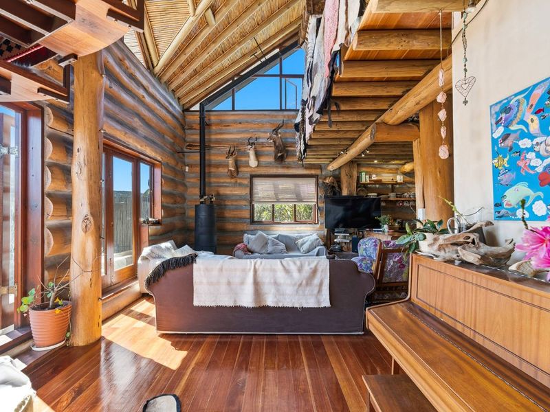 Spacious living room featuring rustic log walls, vaulted timber ceilings, hardwood flooring, and a wood-burning stove with large windows offering natural light.