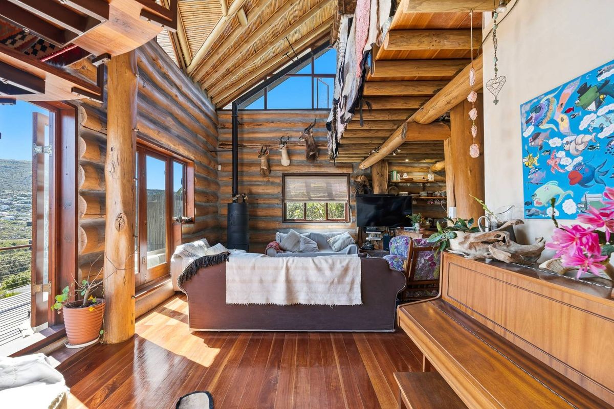 Spacious living room featuring rustic log walls, vaulted timber ceilings, hardwood flooring, and a wood-burning stove with large windows offering natural light.