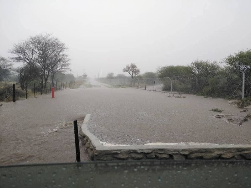 A view of a flooded access road and perimeter fencing on a vacant residential property during heavy rain.