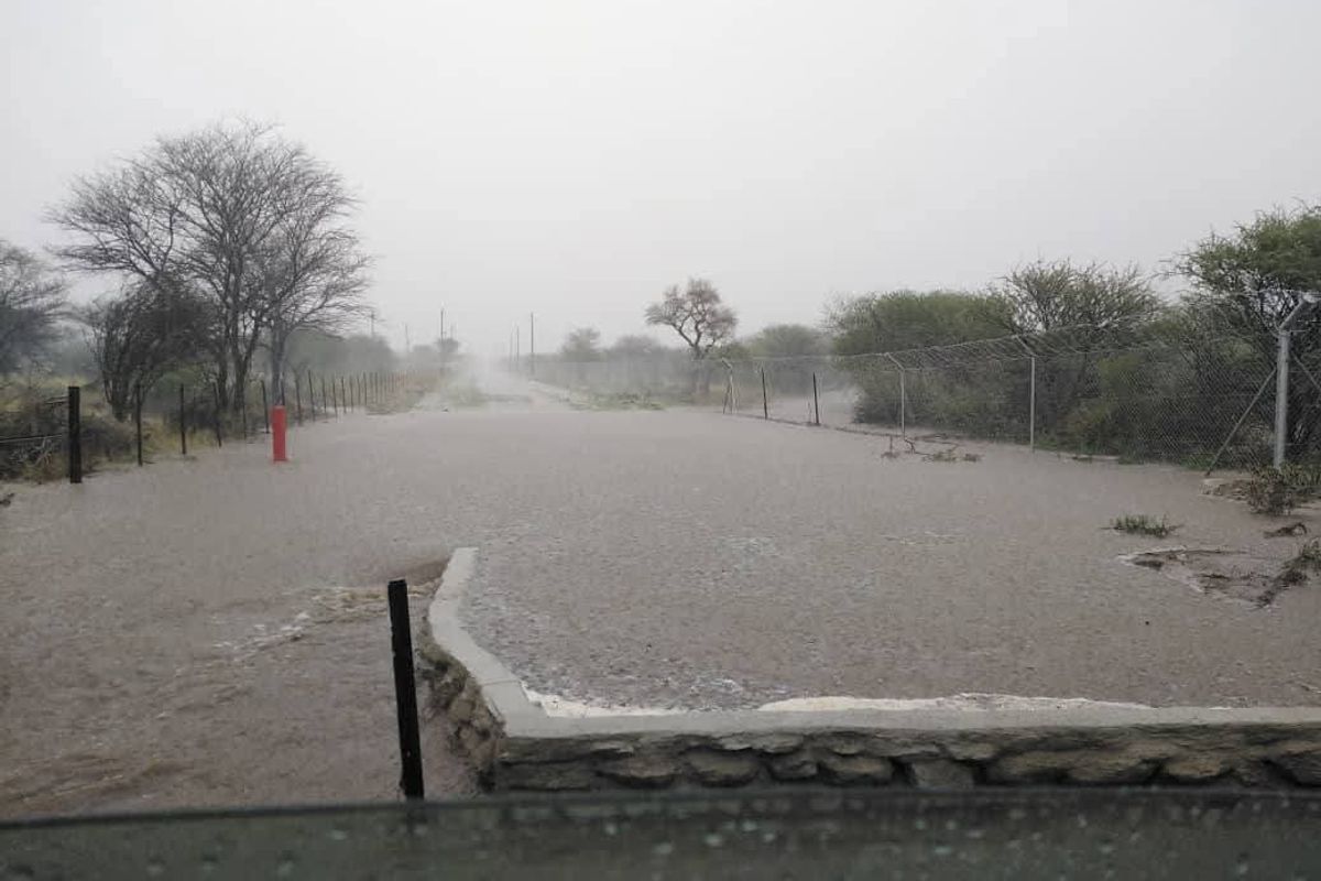 A view of a flooded access road and perimeter fencing on a vacant residential property during heavy rain.