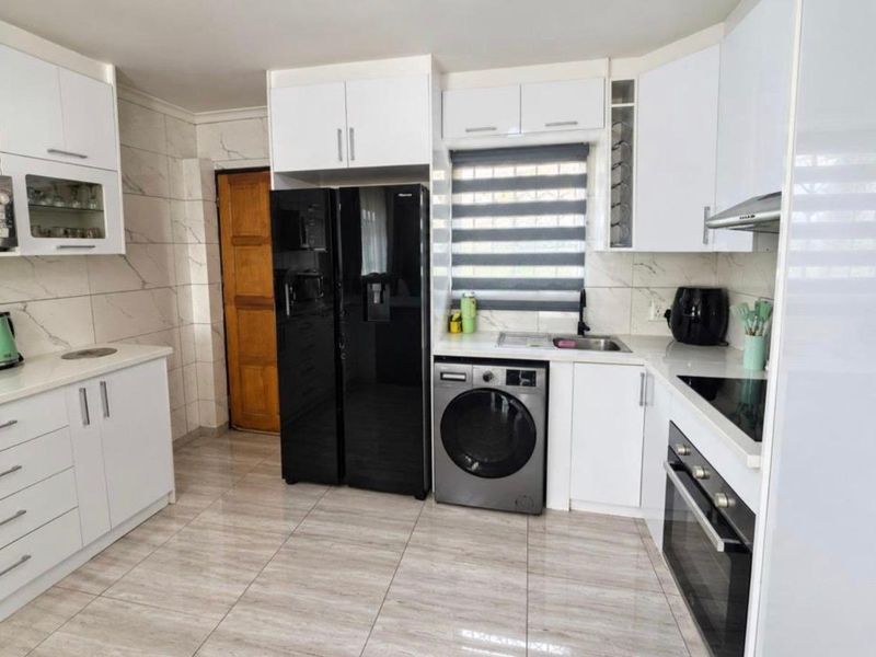 Modern kitchen featuring white cabinetry, marble-look wall tiling, ceramic flooring, and integrated appliances including an oven, hob, and extractor fan.