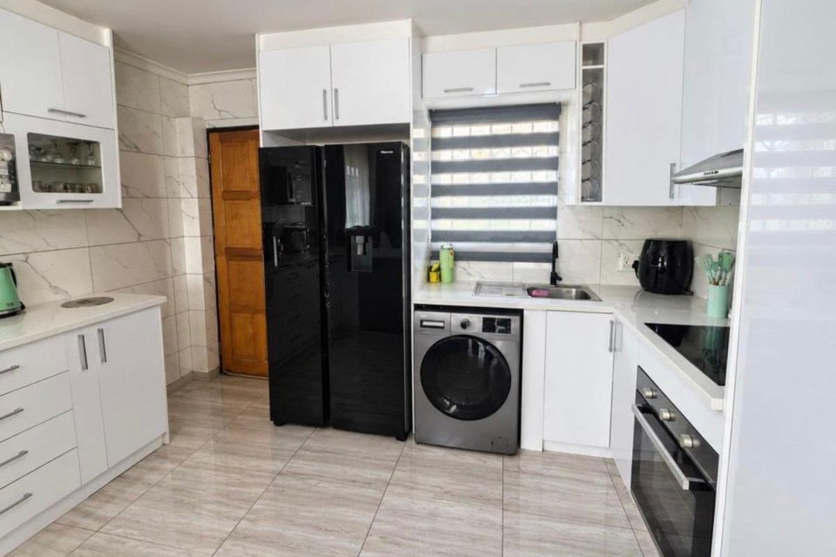 Modern kitchen featuring white cabinetry, marble-look wall tiling, ceramic flooring, and integrated appliances including an oven, hob, and extractor fan.
