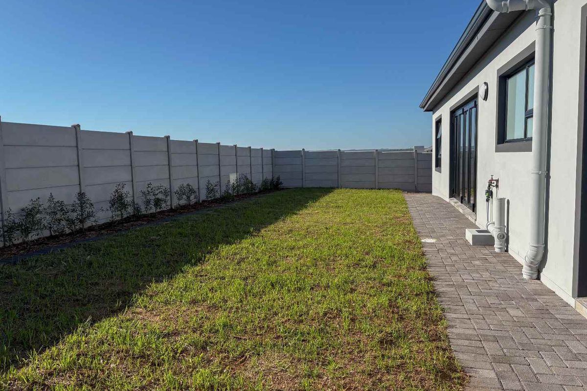 A well-maintained rear garden featuring a paved walkway, lawn area, and perimeter precast concrete walling.