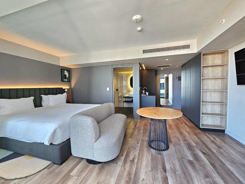 Modern bedroom featuring integrated cabinetry, wood-look flooring, recessed ceiling lighting, and an en-suite bathroom with contemporary finishes.