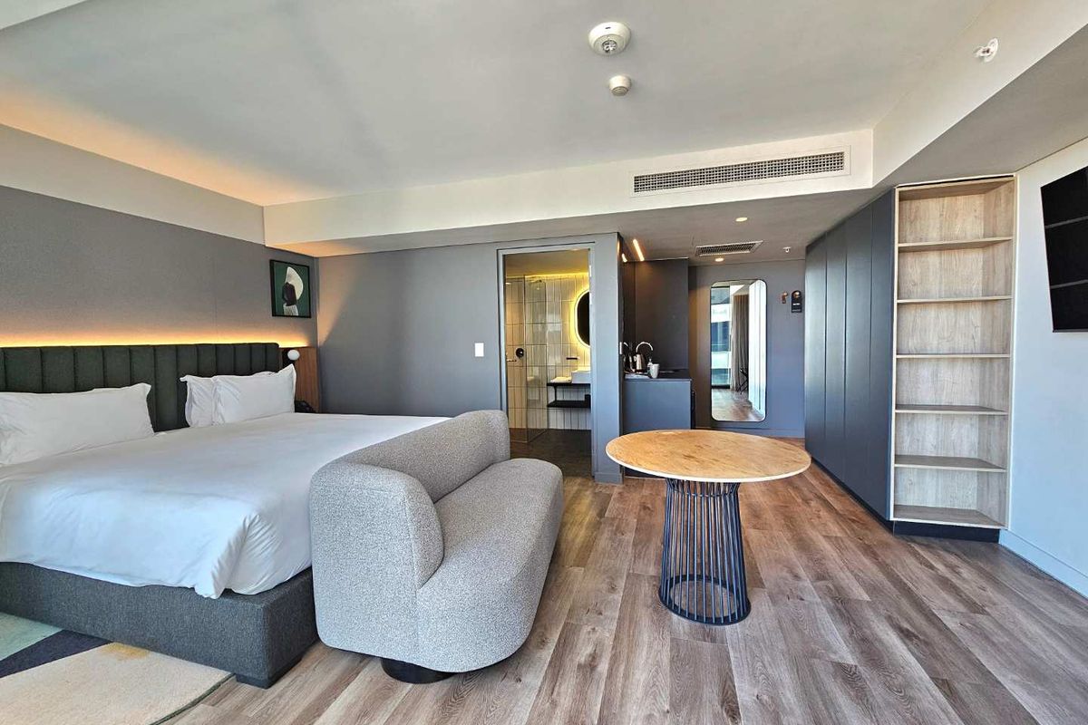 Modern bedroom featuring integrated cabinetry, wood-look flooring, recessed ceiling lighting, and an en-suite bathroom with contemporary finishes.