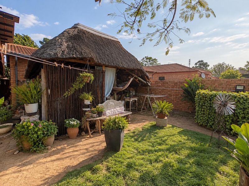 A rear garden area featuring a traditional thatch-roofed lapa structure and brick boundary walling, set within a residential backyard.