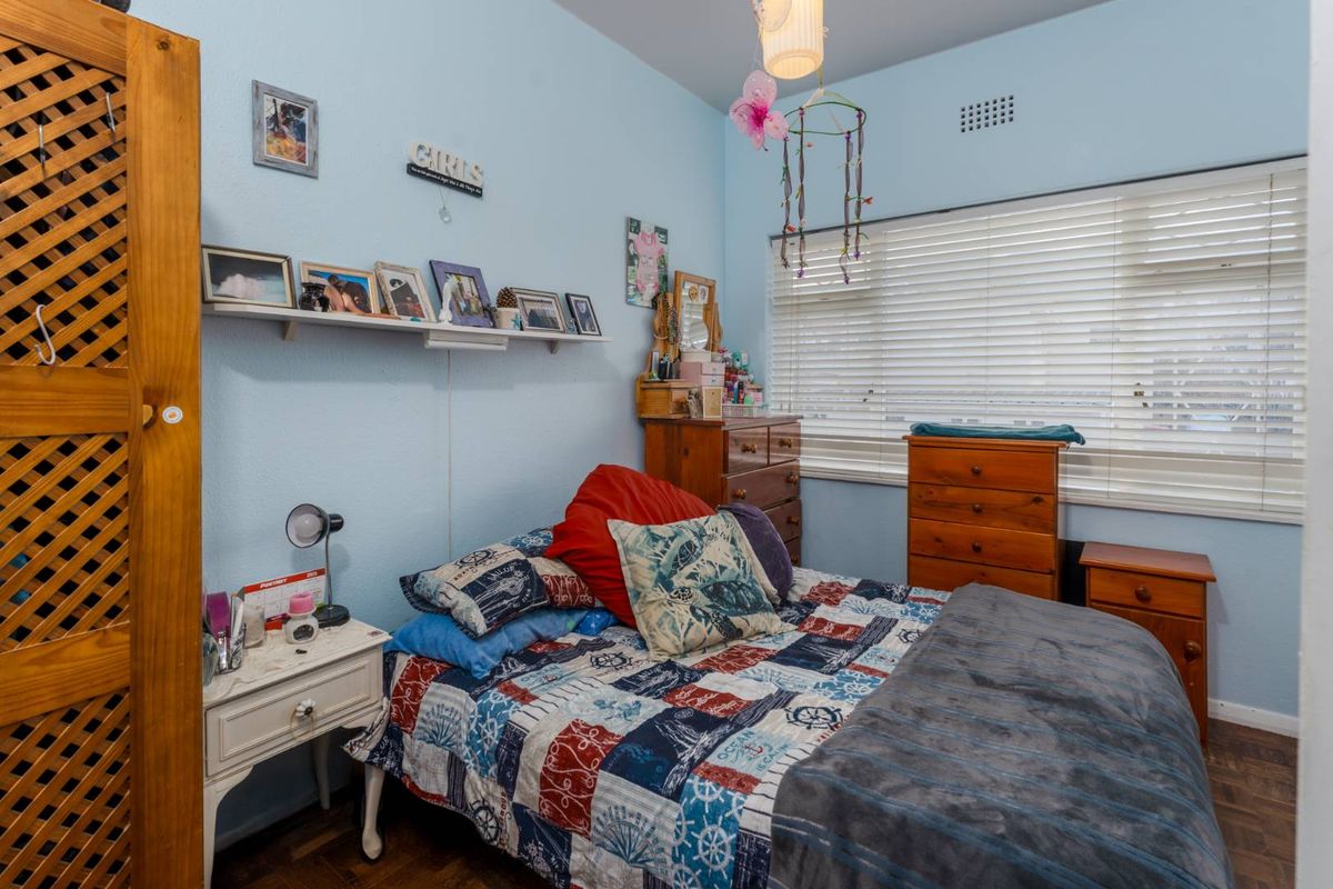 A bedroom featuring parquet flooring, a large window with fitted blinds, and a wall-mounted shelf.