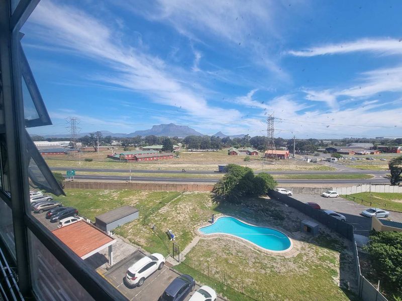 Elevated view overlooking the complex swimming pool, parking area, and surrounding landscape with distant mountain scenery.