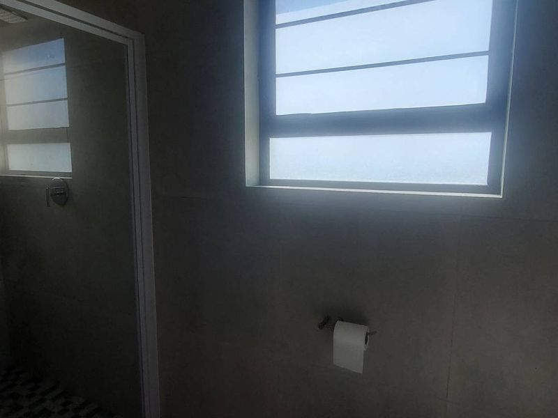 A modern bathroom featuring tiled walls, a shower enclosure, and a window, presenting a clean and functional space.