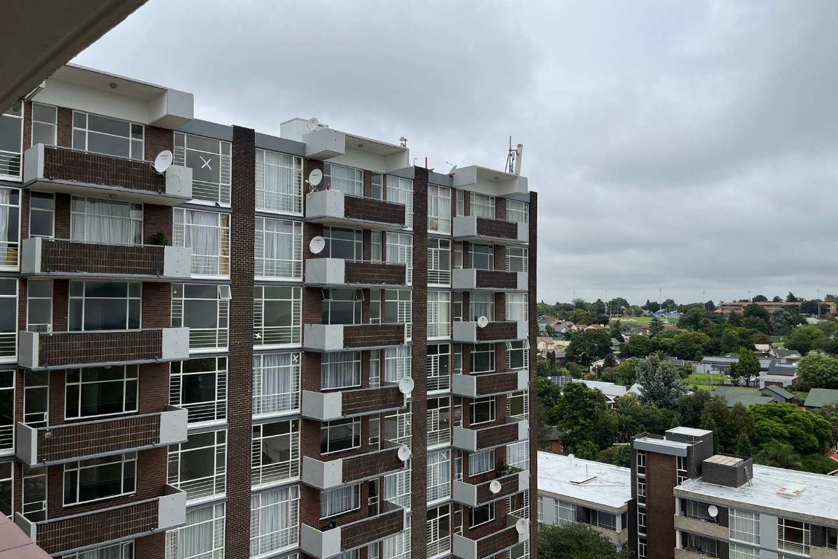 An elevated exterior view of a multi-story apartment building featuring brick cladding, private balconies, and aluminium-framed windows overlooking a suburban landscape.