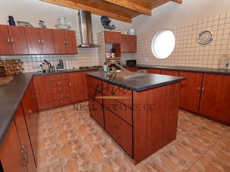 A functional kitchen featuring wooden cabinetry, a central island, tiled backsplash, and exposed timber ceiling beams, offering a classic layout with ample storage space.