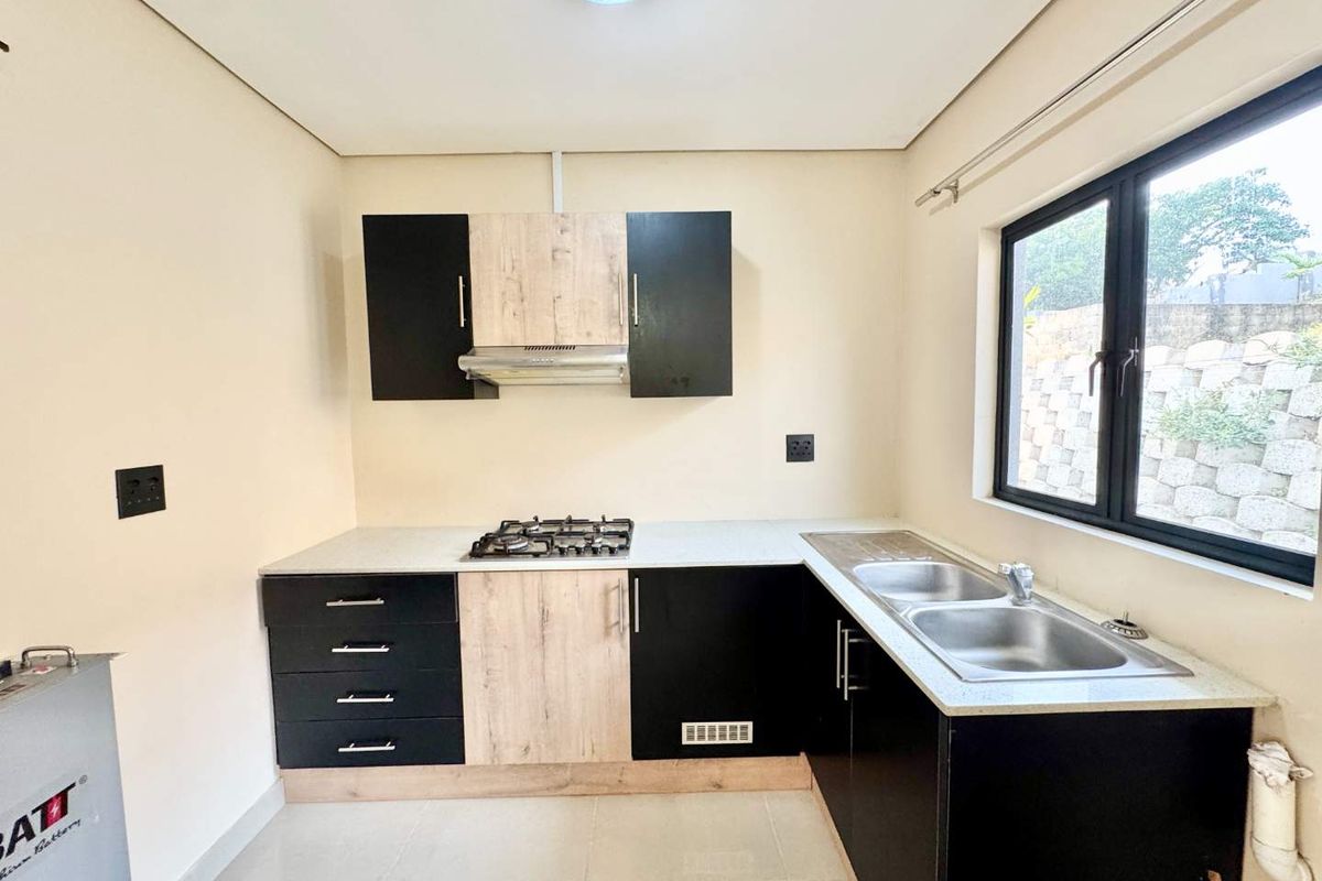 Modern kitchen featuring two-tone cabinetry, a built-in gas hob with extractor fan, and a double stainless steel sink under a large window.