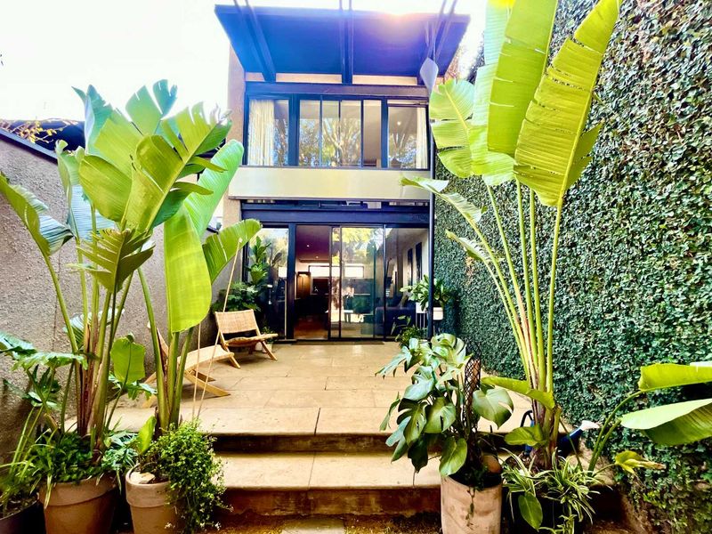 A private rear courtyard featuring a stone-paved patio, lush vertical garden wall, and large sliding glass doors providing seamless indoor-outdoor flow.