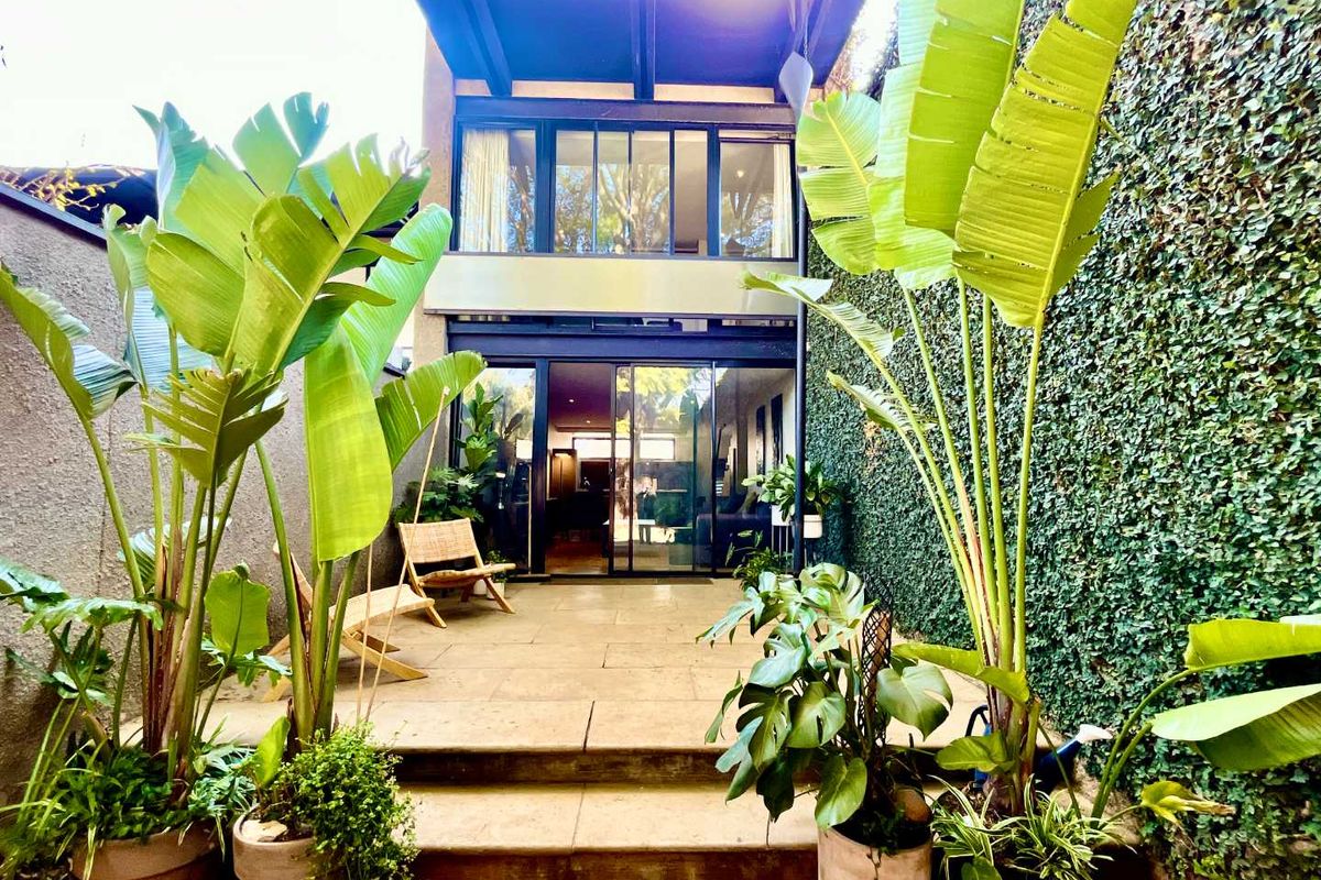 A private rear courtyard featuring a stone-paved patio, lush vertical garden wall, and large sliding glass doors providing seamless indoor-outdoor flow.