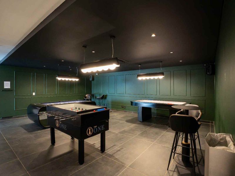 A modern, well-maintained clubhouse games room featuring dark green wainscoting, tiled flooring, and contemporary pendant lighting.