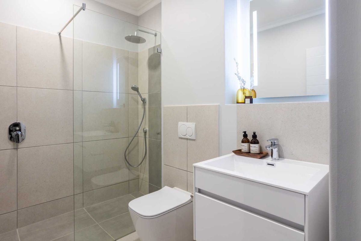 Modern bathroom featuring a walk-in glass shower, wall-mounted toilet, and a sleek vanity with an integrated basin and illuminated mirror.