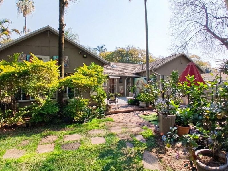 Rear view of the house featuring a landscaped garden, mature trees, and a brick-paved pathway leading to the patio area.
