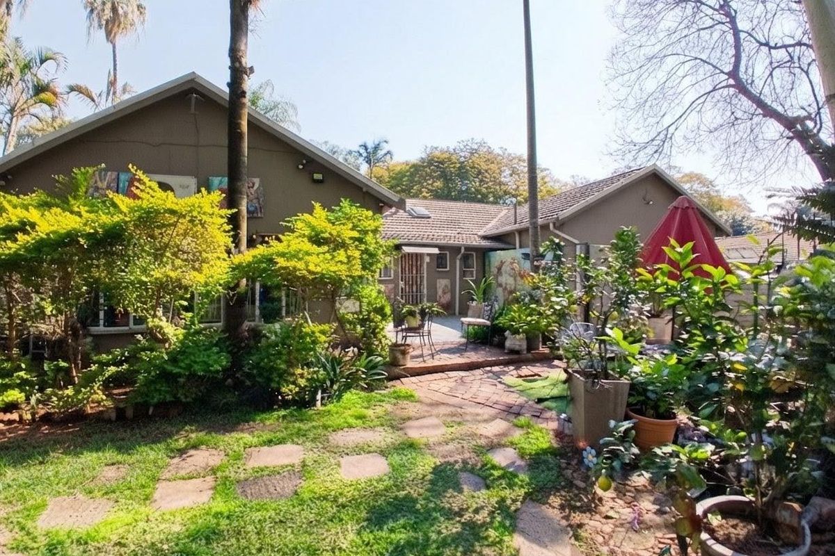 Rear view of the house featuring a landscaped garden, mature trees, and a brick-paved pathway leading to the patio area.