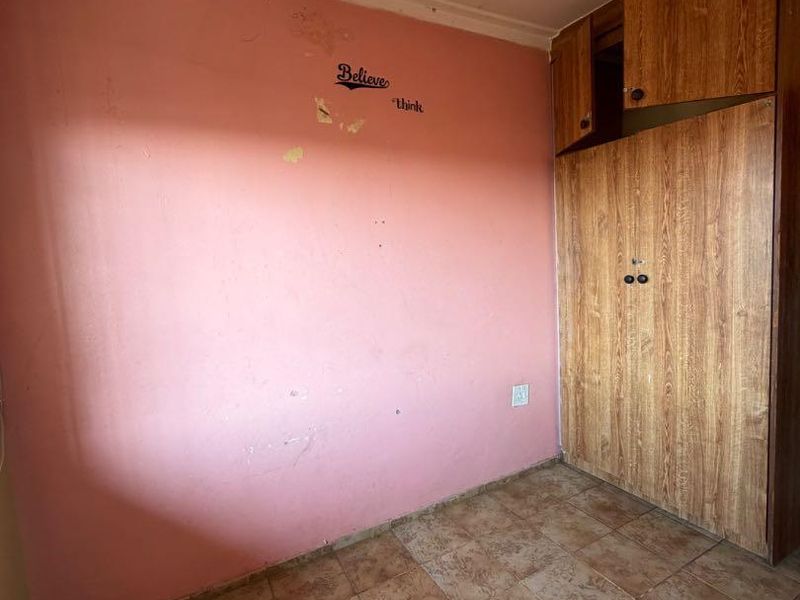 A vacant bedroom featuring built-in wooden wardrobes, tiled flooring, and pink walls requiring cosmetic attention and repainting.