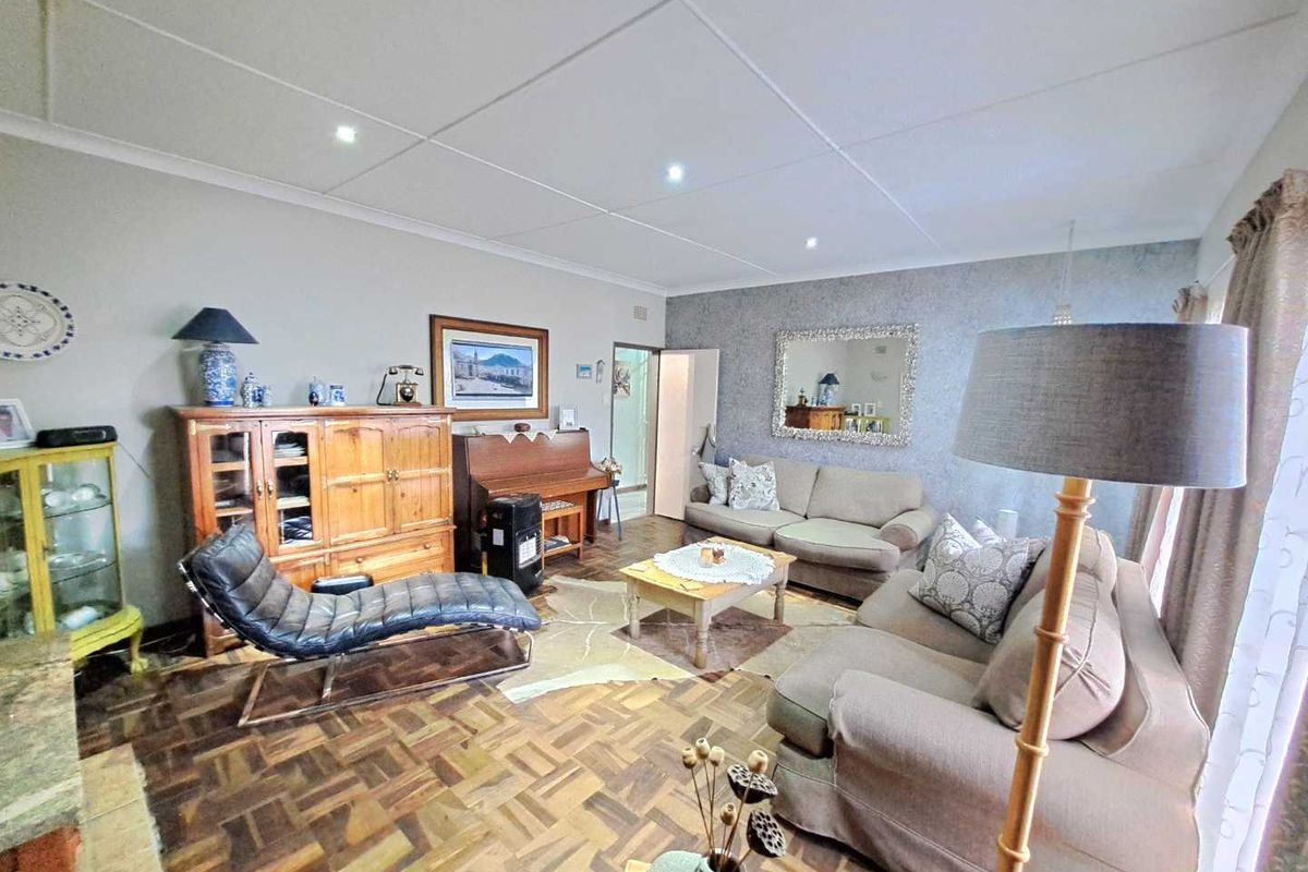 A spacious living room featuring classic parquet flooring, recessed downlighting, and a textured feature wall, offering a comfortable and traditional living space.