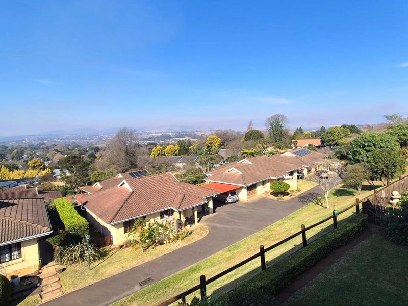 An elevated view overlooking a residential complex with tiled roofs, paved driveways, and landscaped gardens under a clear blue sky.