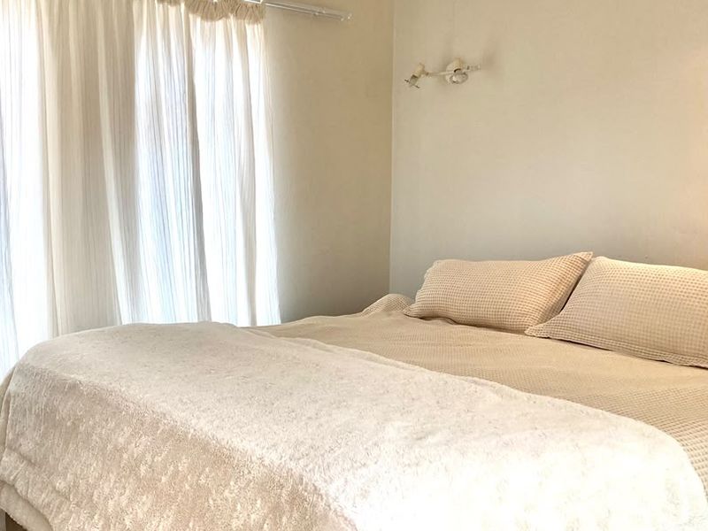 A neutrally decorated bedroom featuring a wall-mounted light fixture and window curtain rod, providing a simple and functional living space.