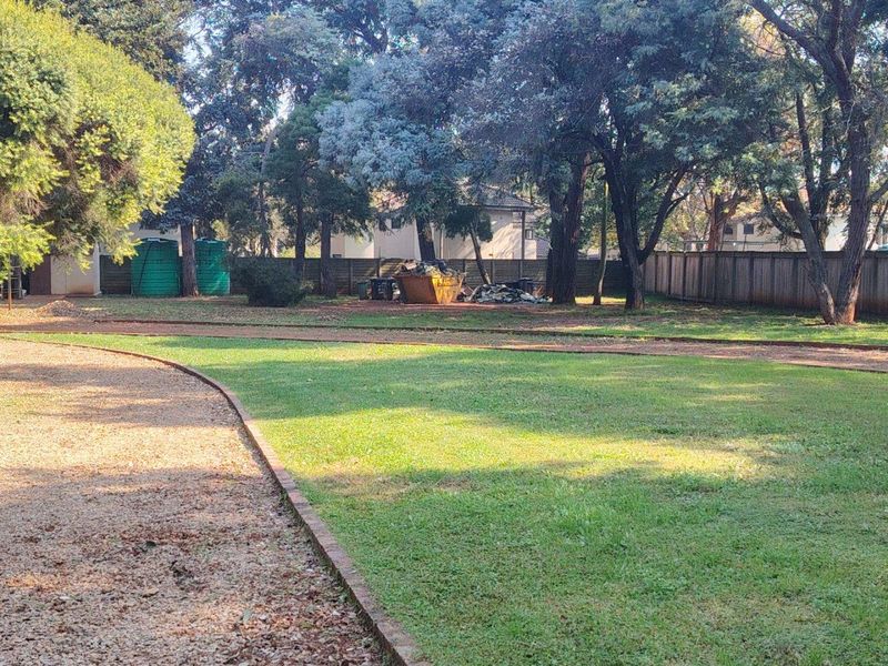 Spacious garden area featuring mature trees, gravel driveway, brick edging, and perimeter timber fencing with installed water storage tanks.