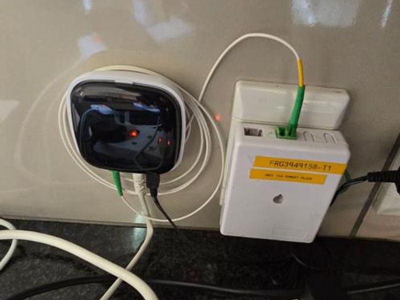 Close-up view of a fiber optic internet terminal and electrical power point mounted on a tiled wall surface.