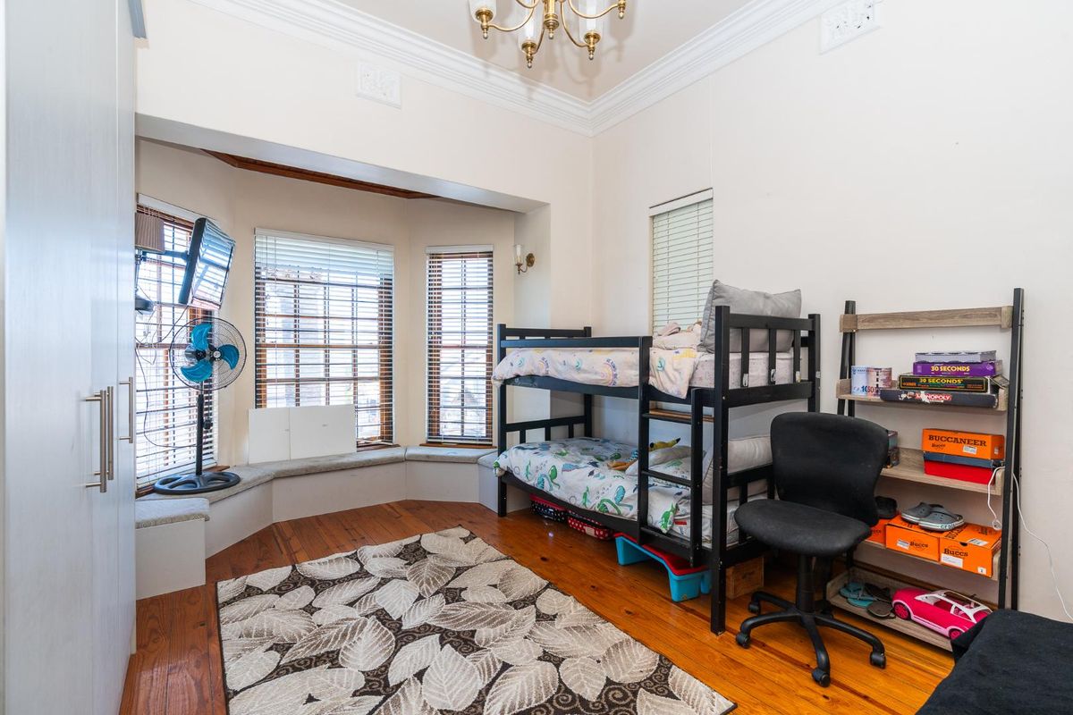 A well-lit bedroom featuring polished timber flooring, a charming bay window with a built-in window seat, and ample built-in wardrobe storage.