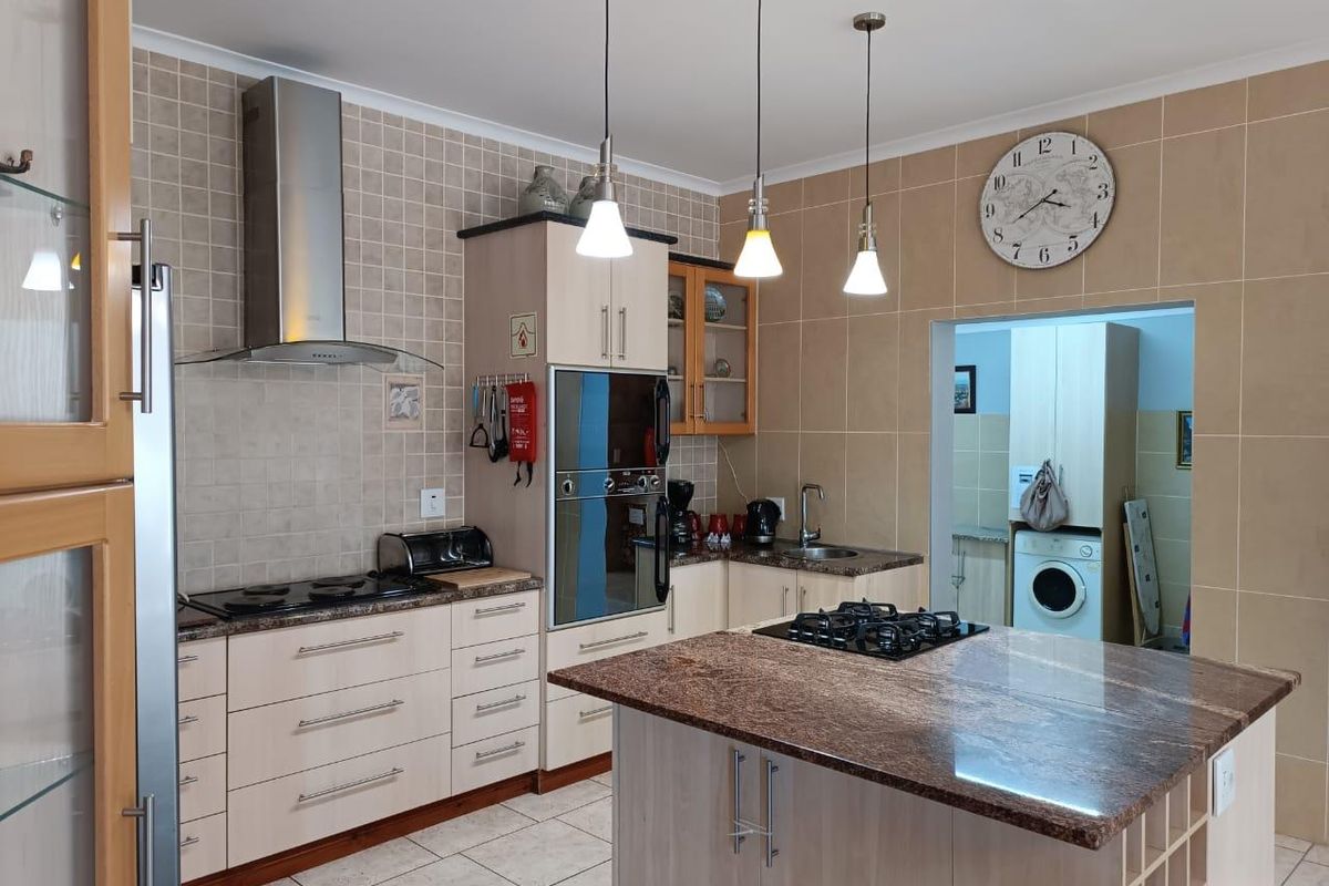 A functional kitchen featuring granite countertops, a central island with a gas hob, built-in oven, and ample cabinetry, with an adjacent scullery area.