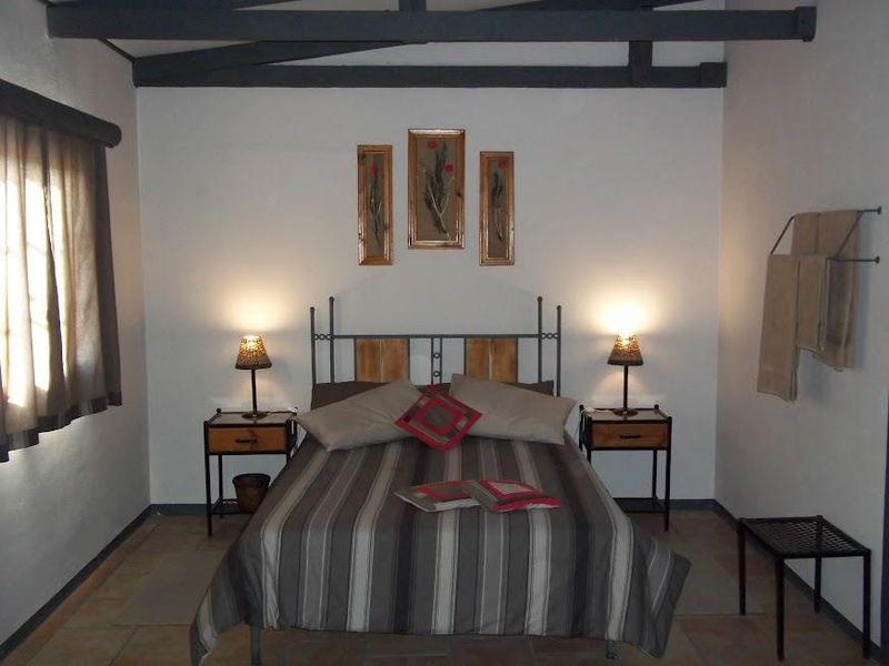 A rustic bedroom featuring exposed timber ceiling beams, tiled flooring, and a neutral color palette, offering a cozy and functional living space.