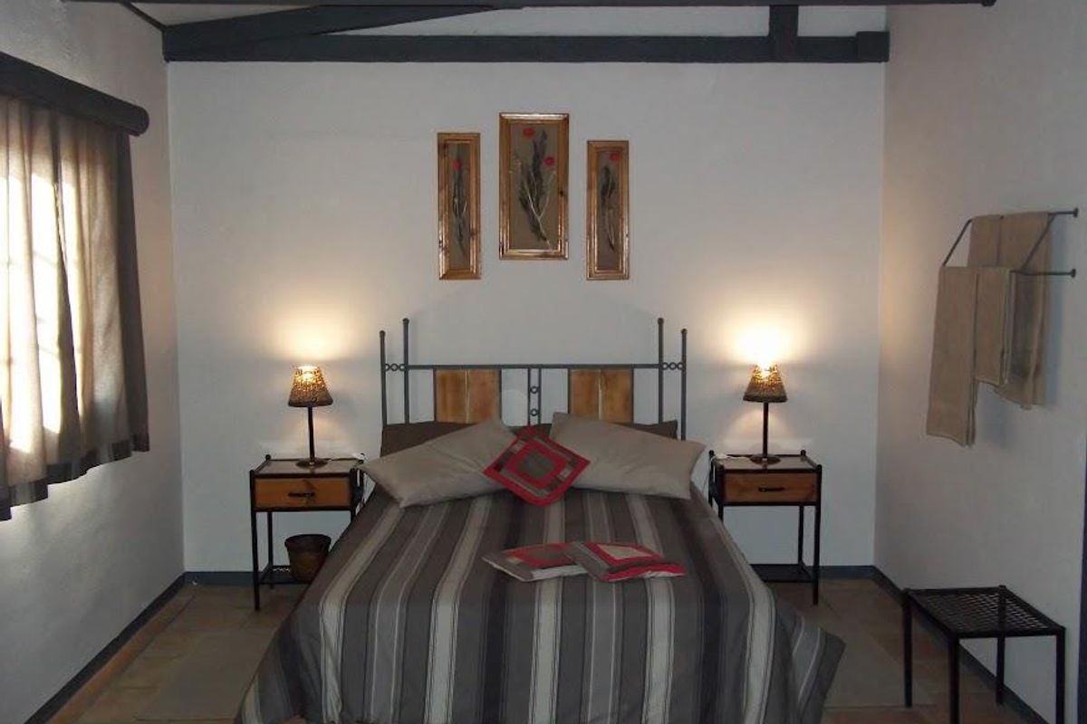 A rustic bedroom featuring exposed timber ceiling beams, tiled flooring, and a neutral color palette, offering a cozy and functional living space.