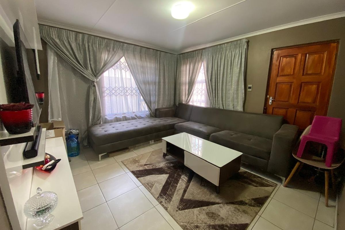 A comfortable living room featuring tiled flooring, large windows with curtain treatments, and a solid timber door.