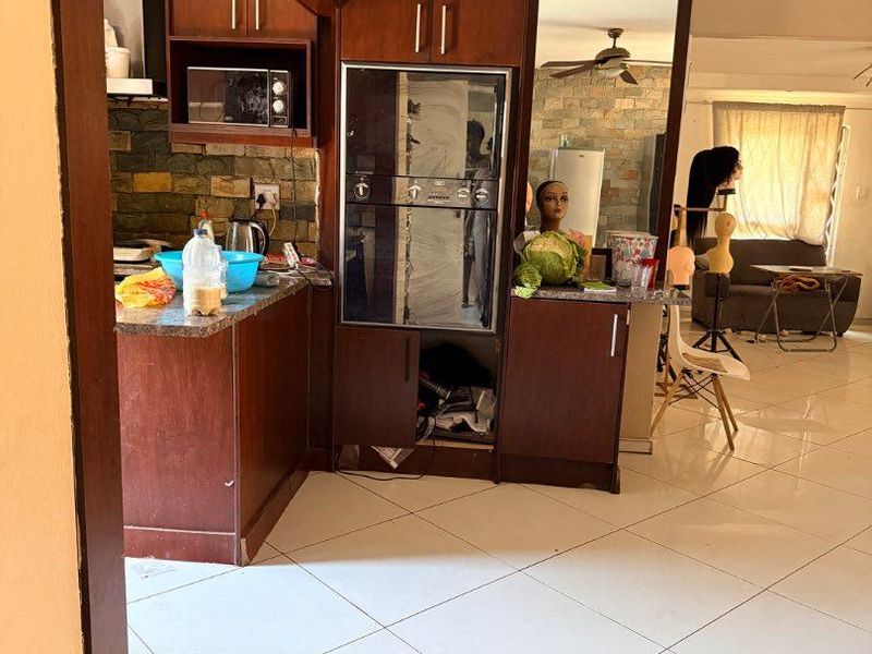 Open plan kitchen and living area featuring dark wood cabinetry, stone countertops, and tiled flooring, offering a functional layout with integrated oven.