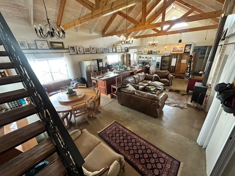 Spacious open-plan living area featuring vaulted ceilings with exposed timber trusses, a central kitchen island, and a cozy wood-burning fireplace.