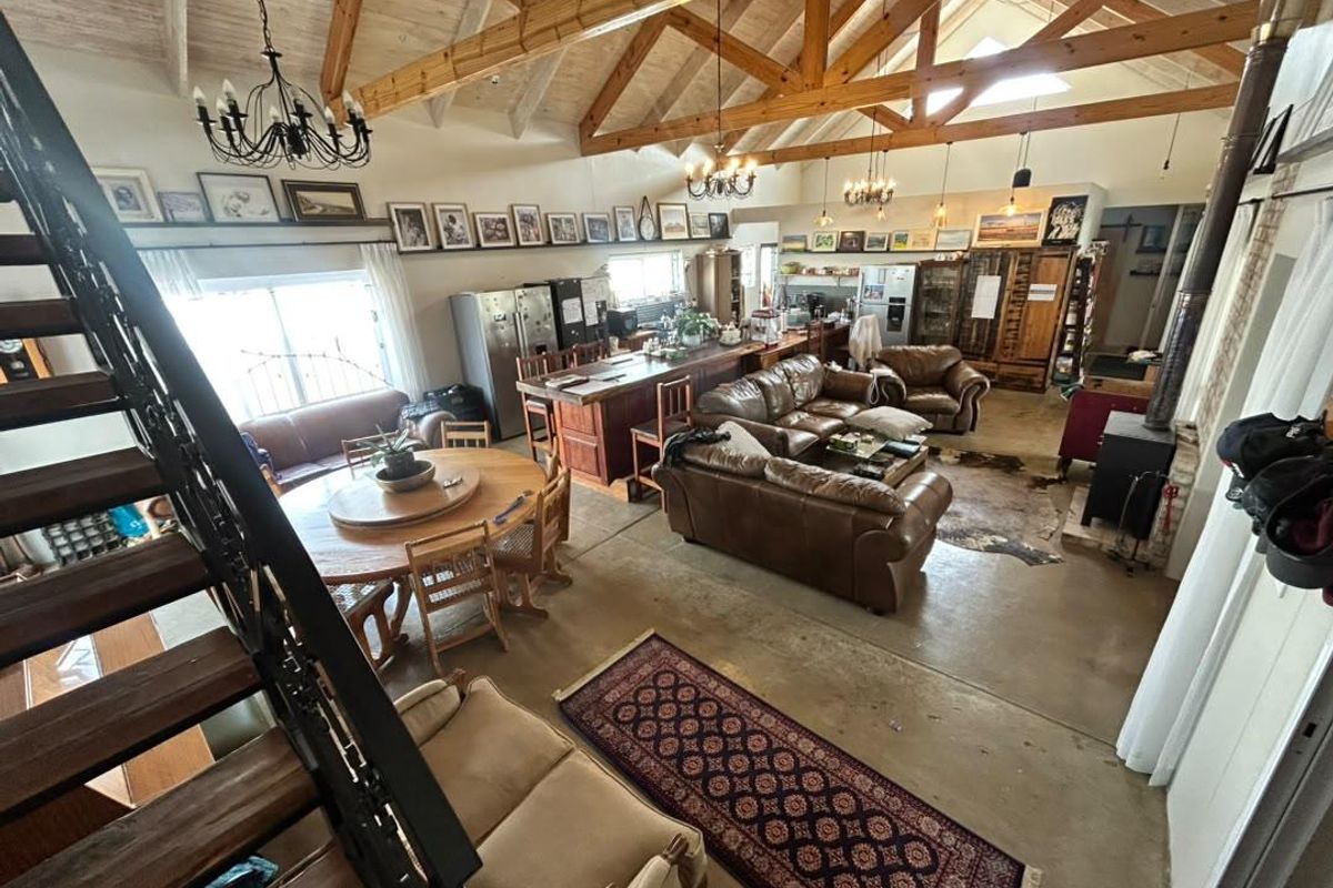 Spacious open-plan living area featuring vaulted ceilings with exposed timber trusses, a central kitchen island, and a cozy wood-burning fireplace.