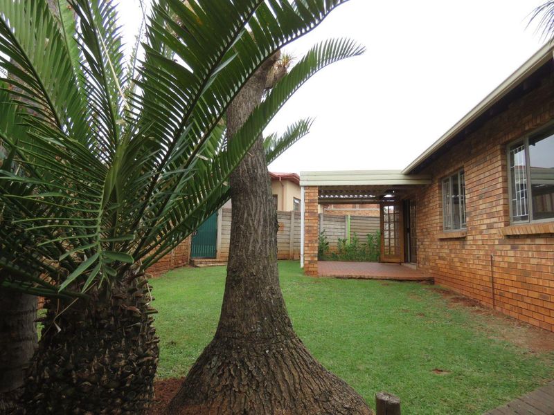 A rear view of the townhouse featuring a brick facade, a covered patio area, and a private garden with established landscaping.
