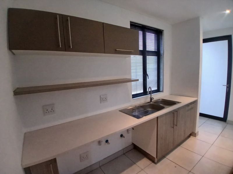 A clean, modern kitchen area featuring built-in cabinetry, a double bowl sink, and neutral tiled flooring, offering a functional and well-maintained workspace.