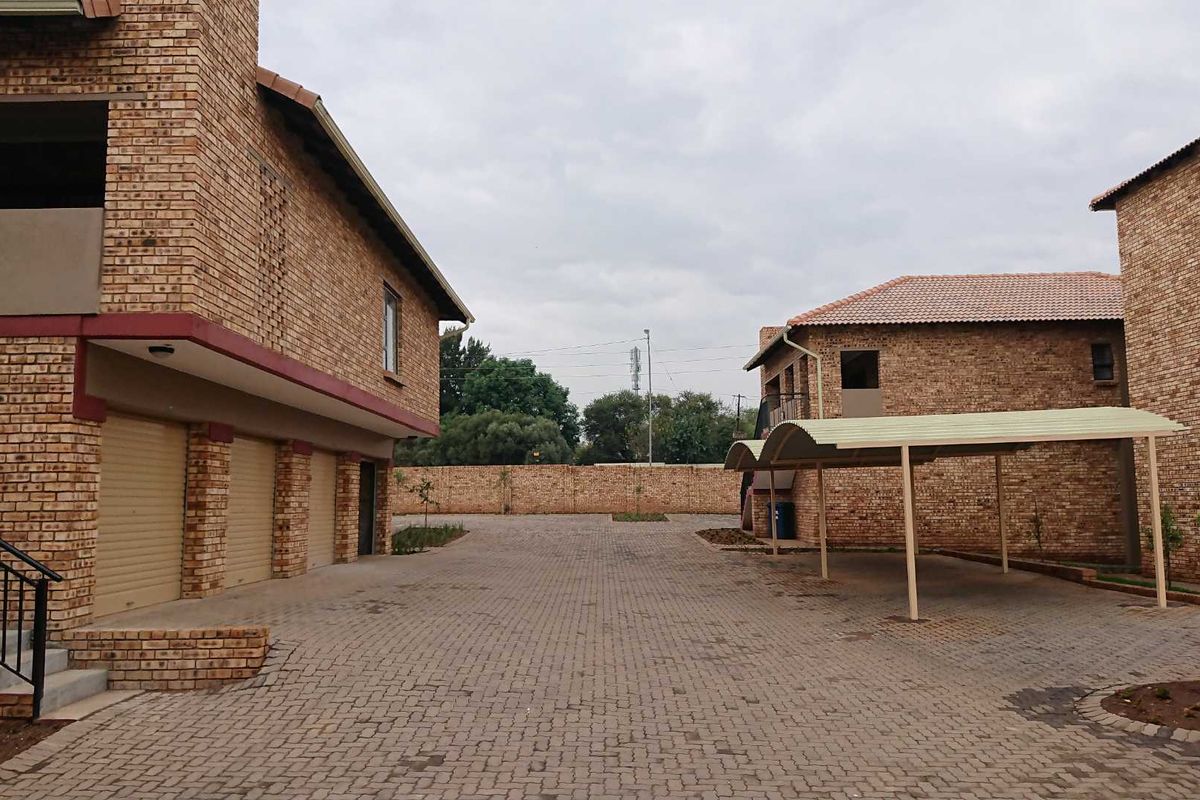 Exterior view of the apartment complex featuring face brick buildings, a paved driveway, and covered carport parking spaces.
