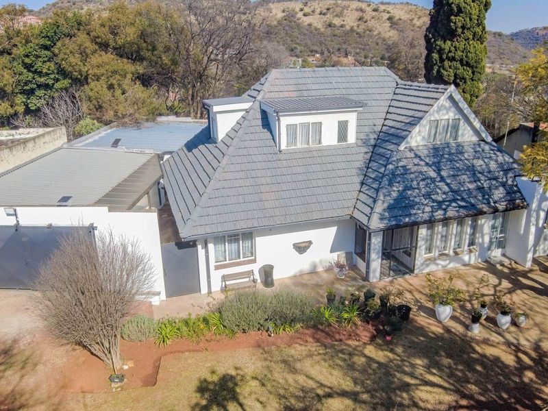 An aerial view of a residential property featuring a tiled roof, dormer windows, a garage, and a landscaped garden area.