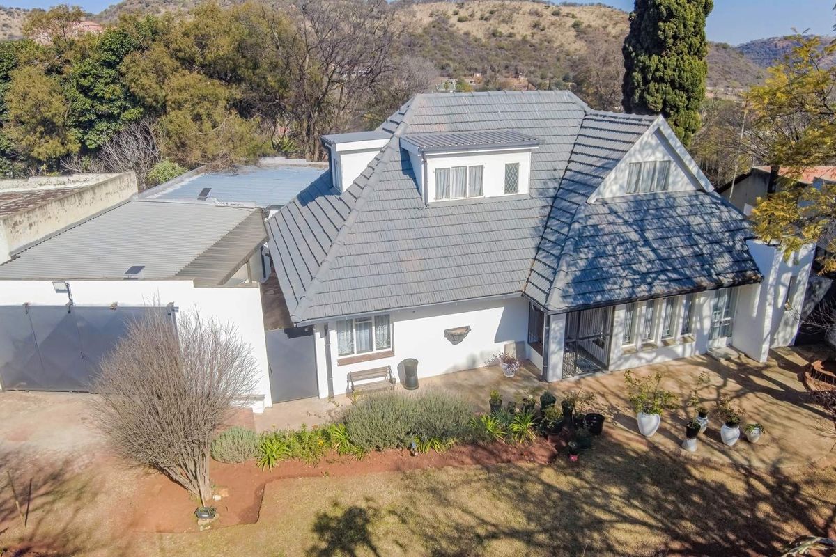 An aerial view of a residential property featuring a tiled roof, dormer windows, a garage, and a landscaped garden area.