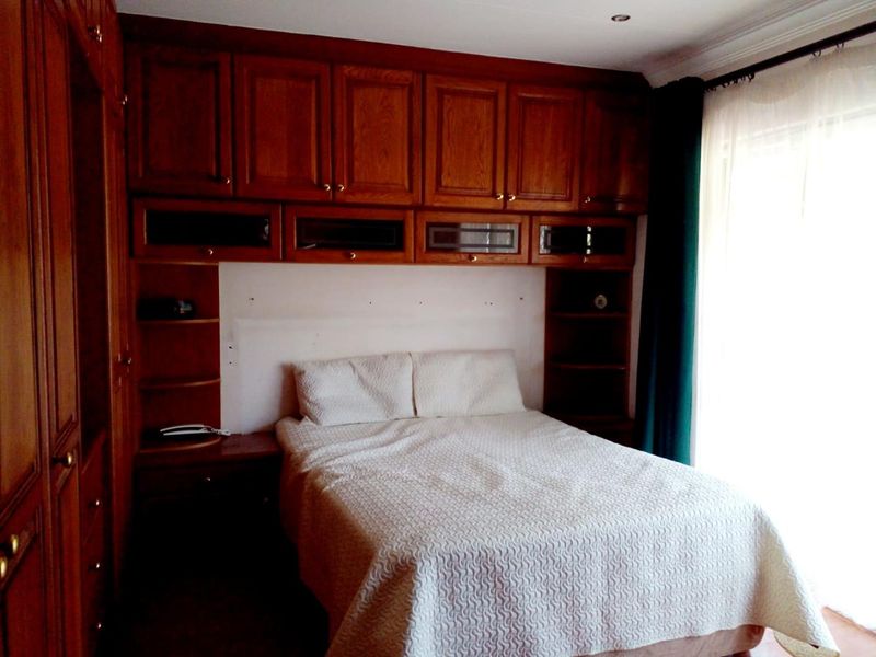 A bedroom featuring extensive built-in wooden cabinetry and storage units surrounding the bed area, with recessed ceiling lighting and classic coving.