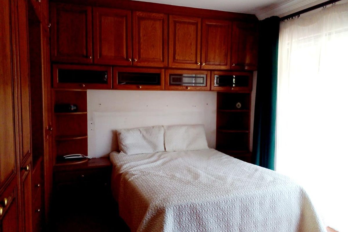 A bedroom featuring extensive built-in wooden cabinetry and storage units surrounding the bed area, with recessed ceiling lighting and classic coving.
